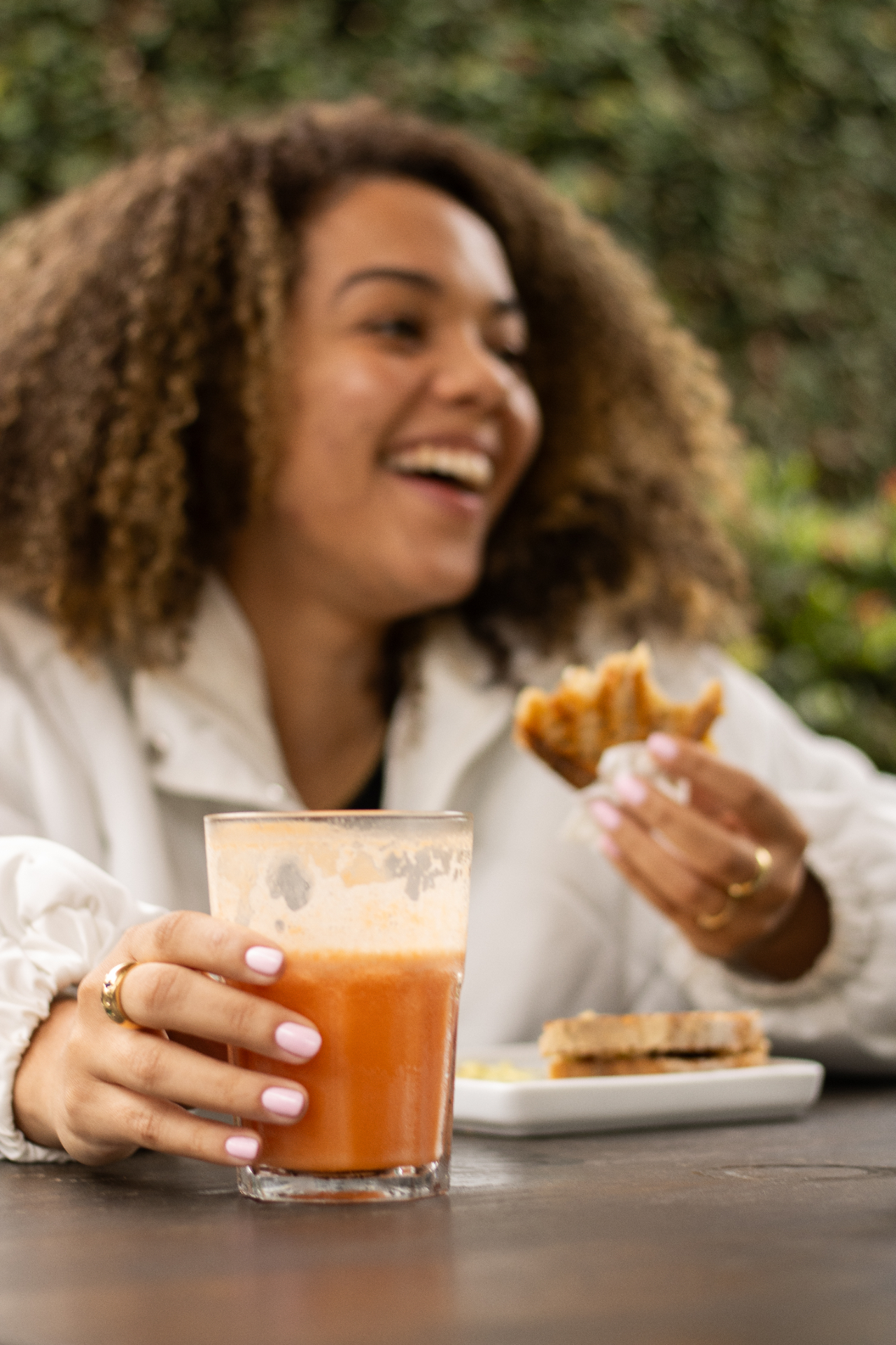 Cliente do Yarn sorrindo, segurando copo de suco natural com sanduíche prensado ao lado, em conversa descontraída.