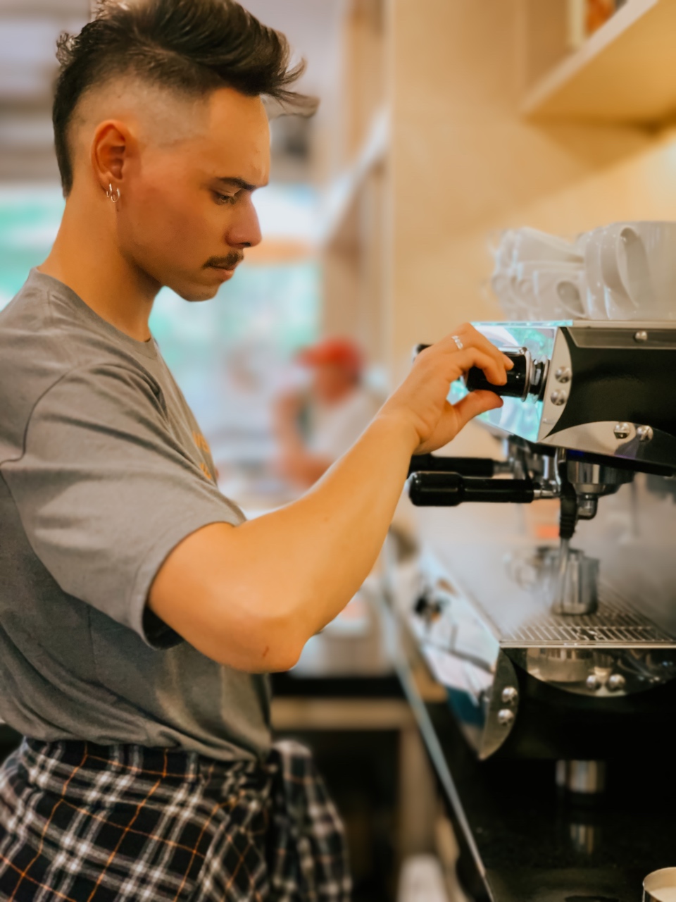 Barista do Yarn ajustando a máquina de espresso, com xícaras empilhadas ao lado.