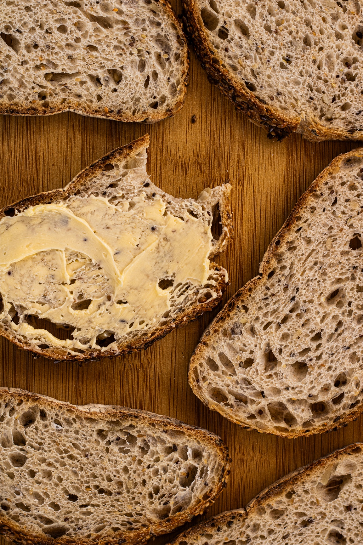 Fatias de pão de fermentação natural com miolo aberto e crosta rústica, uma delas com manteiga espalhada sobre tábua de madeira